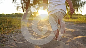 Baby run in the park on the sand. Bare feet child son run on the sand in the park near the water. Happy family kid dream