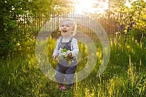 Baby`s first independent steps in the garden in sunlight. Cute summer blond girl laughing in the garden.