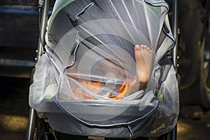 The baby`s foot rested against the mosquito net on the stroller