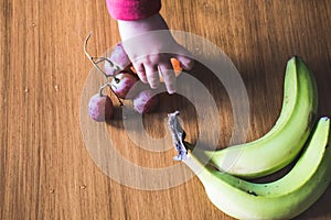 Baby s hand manipulating different fruits on a wooden table