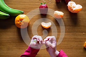 Baby s hand manipulating different fruits on a wooden table