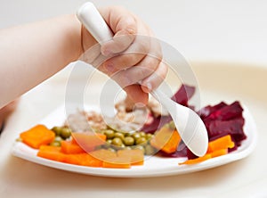 Baby's hand and plate with vegetables