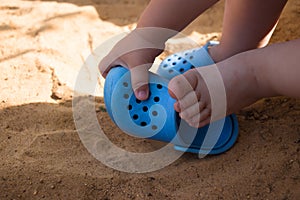 the baby& x27;s legs in the beach sand, blue flip flops and a toy shovel, play in the sandbox