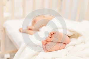 Baby`s legs in focus against the background of a sleeping baby in a white bed, a healthy and calm baby`s sleep