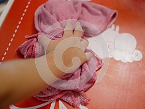 Baby`s little hand with a piece of cloth cleaning a his / her own table