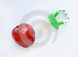 Baby`s nibbler and red apple on white background. Organic baby food concept photo