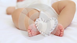 baby's small feet on a white bed with a plush heart, a place for text, close-up of a small child's feet and
