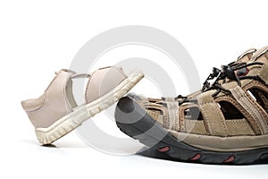 Baby sandal stepping on adult shoe, isolated