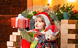 Baby Santa boy holding and looking at Christmas box gift trying to guess what is inside it. Little kid at Santa's