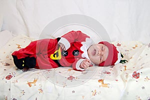Baby in santa claus costume sleeping in bed