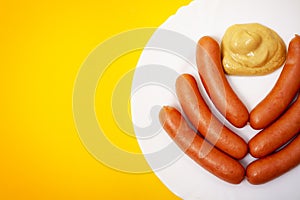 Baby sausages with mustard served on a plate against a yellow background with copy space