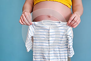 Baby shirt in the hands of a pregnant woman on a blue background