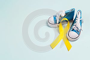 Baby shoes with childhood cancer awareness golden ribbon on blue background with copy space