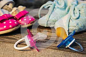 Baby shoes and pacifiers pink and blue on the old wooden background.