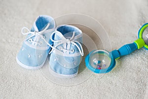 Baby shoes and rattle on light background