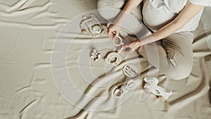 Baby shower, infant care concept. Pregnant woman holding wooden newborn stuff, baby accessories - shoes, toys on beige