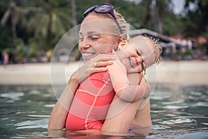 Baby sincerely hugging his mother during beach holidays. Conceptual picture symbolizing baby care and love