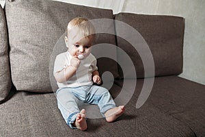 Baby sits on couch with a baby`s dummy in his mouth