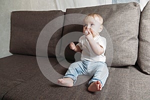 Baby sits on couch with a baby`s dummy in his mouth