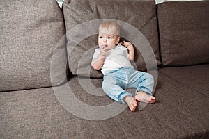 Baby sits on couch with a baby`s dummy in his mouth