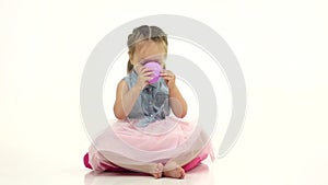 Baby sits on the floor and drinks tea. White background. Slow motion