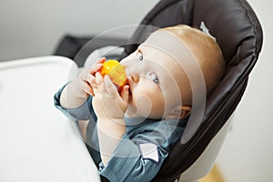 Baby sits in highchair and eats peach