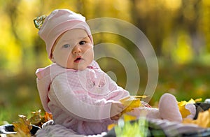 Baby sitting in autumn, fall leaves in park scene.