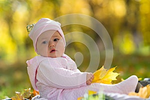 Baby sitting in autumn, fall leaves in park scene.