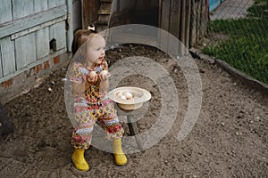 Baby is sitting on a bench by the chicken coop and holding fresh eggs in her hands.