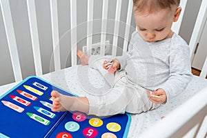 Baby sitting in a crib playing with montessori busy book. Concept of keeping children from screen by activity books and