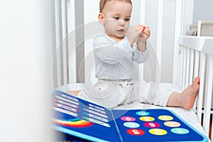 Baby sitting in a crib playing with montessori busy book. Concept of keeping children from screen by activity books and