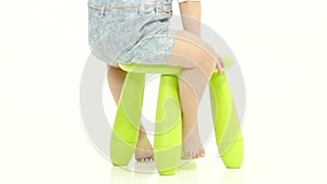 Baby is sitting on a green chair, holding a candy. White background. Slow motion