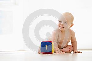 Baby sitting indoors with block smiling