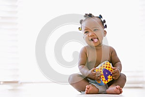 Baby sitting indoors with block smiling