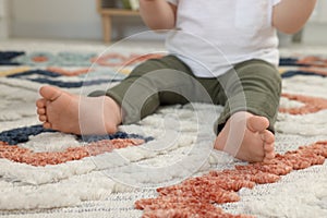 Baby sitting on soft carpet indoors, closeup