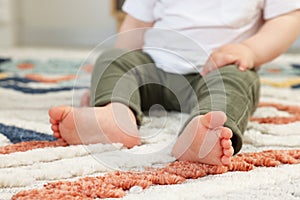 Baby sitting on soft carpet indoors, closeup