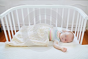 Baby sleeping in co-sleeper crib attached to parents` bed