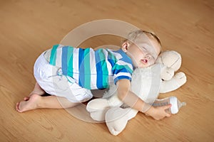 Baby sleeping on floor with toy and milk bottle.