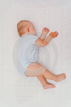 Baby sleeping on its side on a white blanket, top view