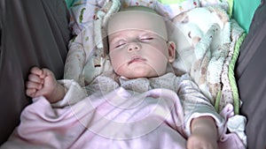 A baby is sleeping with a pacifier in its mouth in a stroller. Face close up.