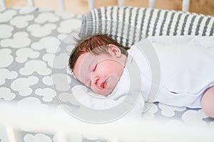 The baby sleeps in the crib. A charming baby sleeps in a crib for sleeping attached to the bed of the parents. A small child