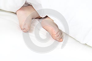 Baby sleeps on a white bed with his feet. Selective focus.