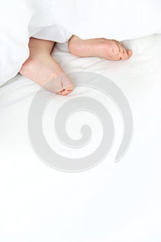 Baby sleeps on a white bed with his feet. Selective focus.