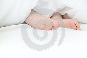 Baby sleeps on a white bed with his feet. Selective focus.