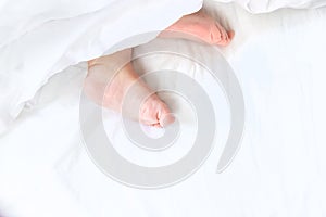 Baby sleeps on a white bed with his feet. Selective focus.