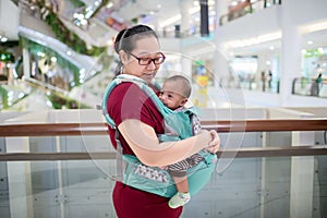 Baby in sling indoor. Little baby boy and her mother walking in department store.