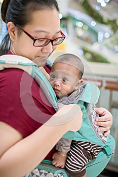 Baby in sling indoor. Little baby boy and her mother walking in department store.