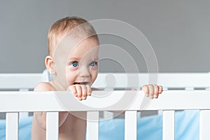 Baby with a sly expression on the face of a little prankster in a white classic crib photo