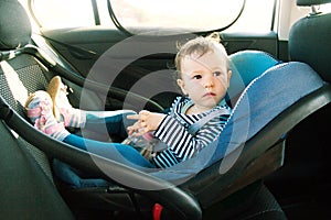 Baby smile in a safety car seat. security. one year old child girl in blue wear sit on auto cradle. Rules for the Safe Transport o