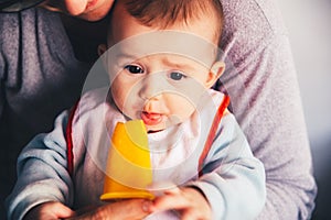 Baby smiling and drooling when trying for the first time an ice cream from his mother`s hands, infant feeding through the baby le